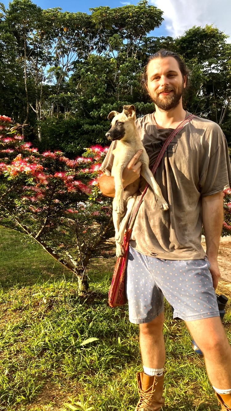 A smiling man holds a puppy in front of a flowering bobinsana bush