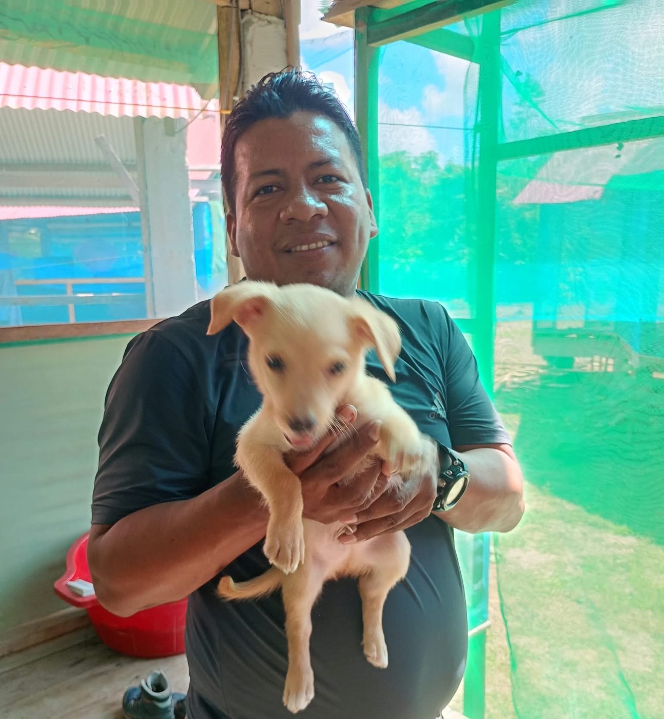 Don Wilder smiling as he holds a small cream-colored puppy on the porch at camp